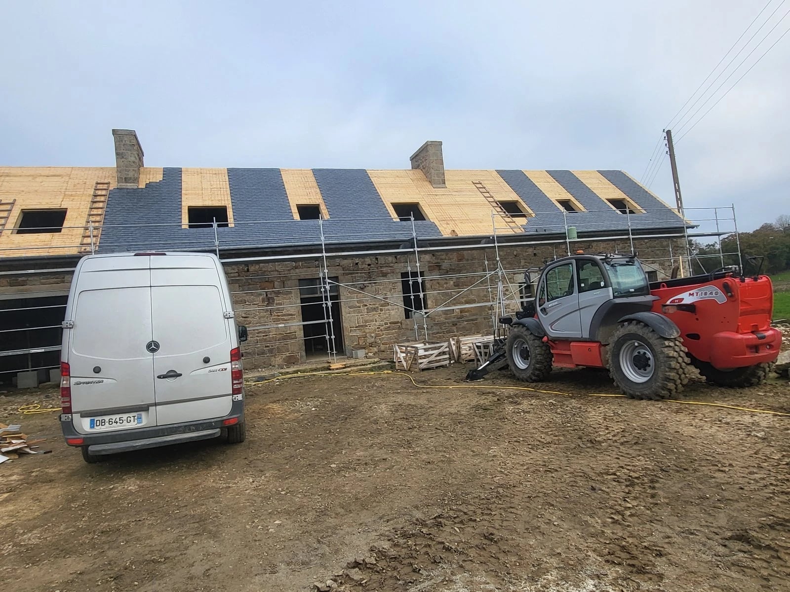 Chantier de couverture en cours, utilitaire et chariot élévateur devant la maison